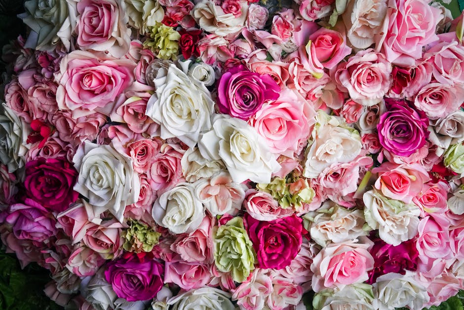 A dense arrangement of fresh roses and lisianthus in shades of pink, white, and deep magenta, with some green hydrangea accents, displayed in a floral shop environment. The roses and lisianthus have s